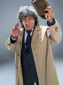 The senior man in cloak as detective or mafia boss. Studio shot on gray in retro stile. Mature man with hat and suitcase