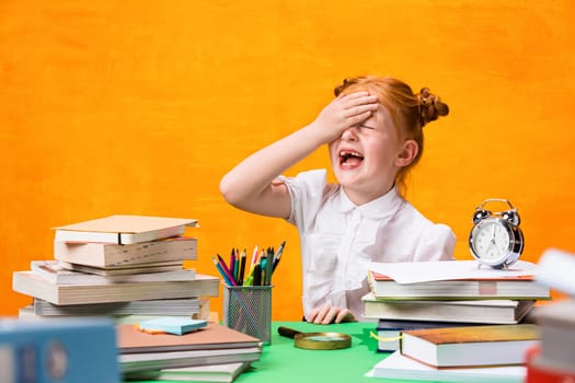 The unhappy teen girl with lot of books sitting at table on orange studio background. The education and back to school concept