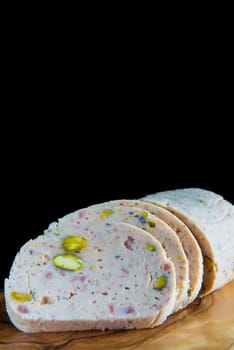 Cold meat made of chicken, bacon and pistachios sliced on a cutting board