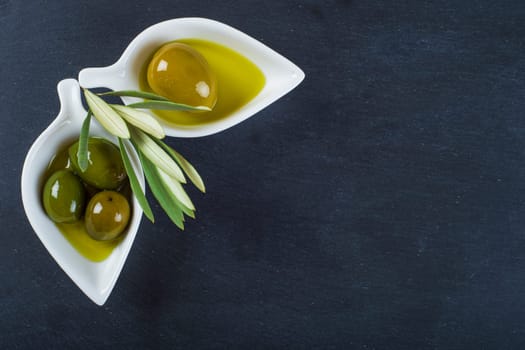 Extra virgin olive oil and green olives on a blackboard with a copy space