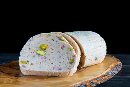 Cold meat made of chicken, bacon and pistachios sliced on a cutting board