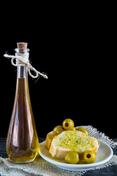 Extra virgin olive oil and bread slices with pitted green olives on a black background