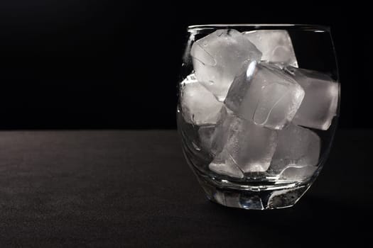Ice cubes in glass on gray and black background.