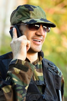 The smiling soldier in uniform is calling, talking, using phone.