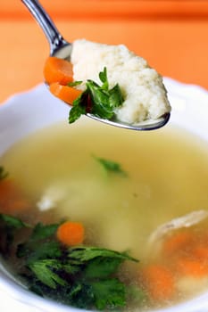 Homemade soup with noodles is in spoon and plate on orange background.