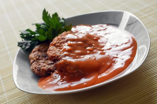 Meatballs in tomato sauce is in white plate on natural background.