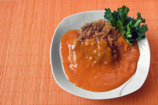 Meatballs in tomato sauce is in white plate on orange background.