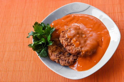 Meatballs in tomato sauce is in white plate on orange background.