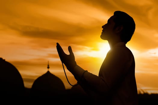 Silhouette of asian muslim man raising hand and praying during sunset background