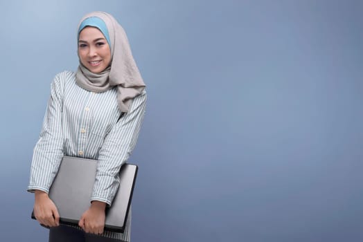 Young asian muslim woman holding laptop against bright background