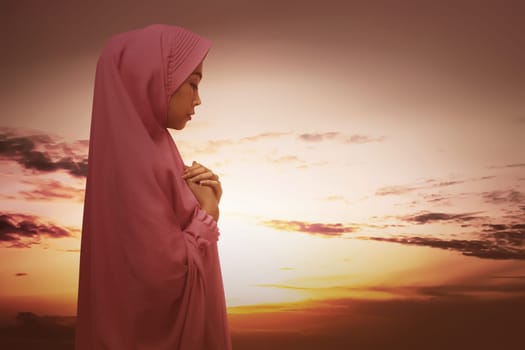 Beautiful asian muslim woman with hijab praying against sunset at sky