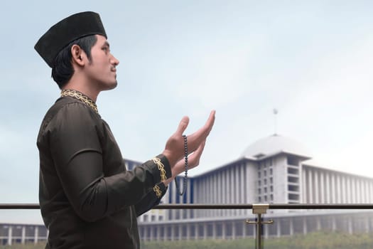 Religious asian muslim man in traidional dress praying to god with mosque backgroud