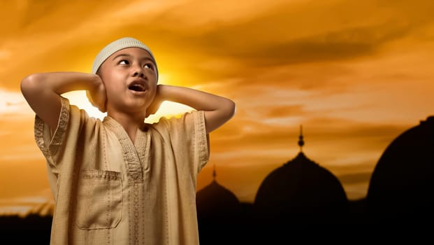 Little asian muslim boy with cap praying during sunset background