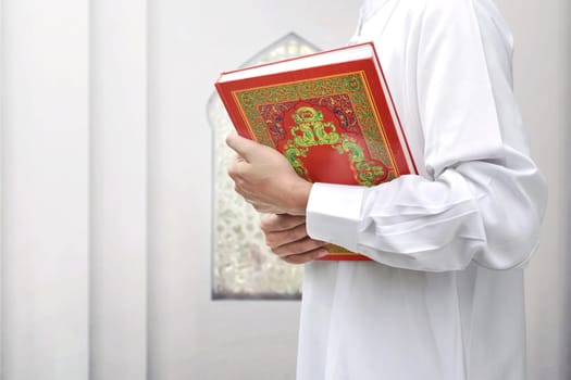 Muslim man with traditional dress holding the Koran inside the mosque