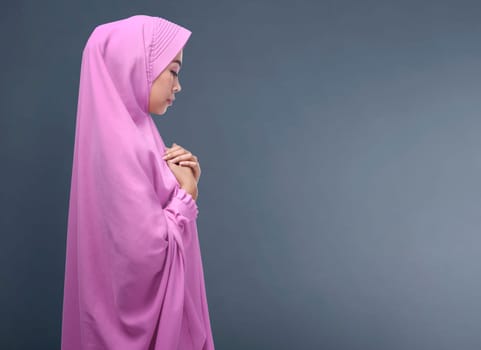 Pretty asian muslim woman with veil praying against dark background