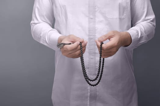 Muslim man praying with prayer beads over dark background