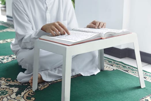 Muslim man sitting on carpet and reading the Koran in the mosque