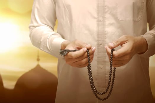 Muslim man holding prayer beads and praying with sunset view background