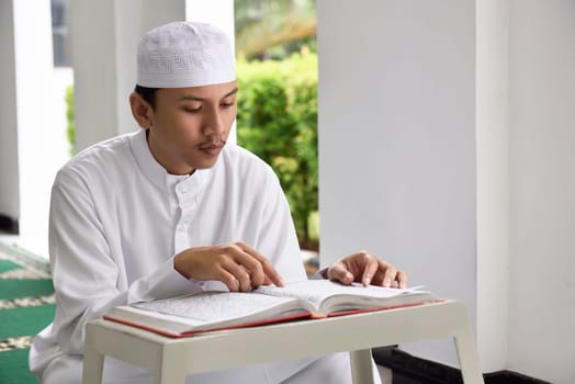 Religion asian muslim man with cap reading holy book Koran on the mosque