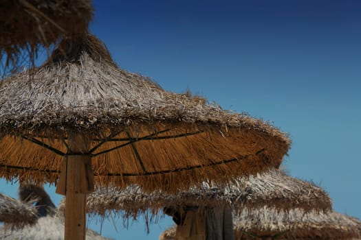 Parasol made of straw or sugar cane produced. Beach sun protection in the background a cloudless blue sky.