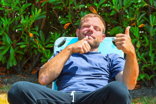 Young man sits in a deck chair and holds his thumbs up.