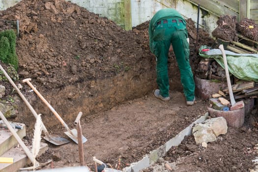 Man digging up soil on an outdoor construction site..