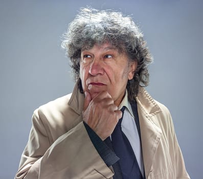 The senior man in cloak as detective or mafia boss. Studio shot on gray in retro stile