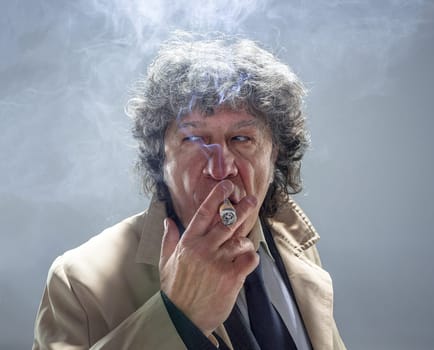 The senior man in cloak with cigar as detective or mafia boss. Studio shot on gray in retro stile