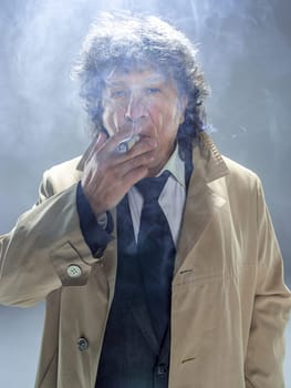 The senior man in cloak with cigar as detective or mafia boss. Studio shot on gray in retro stile