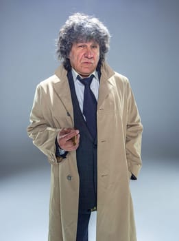 The senior man in cloak with cigar as detective or mafia boss. Studio shot on gray in retro stile