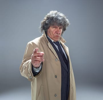 The senior man in cloak as detective or mafia boss. Studio shot on gray in retro stile