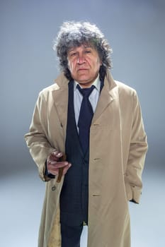 The senior man in cloak with cigar as detective or mafia boss. Studio shot on gray in retro stile
