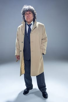 The senior man in cloak with cigar as detective or mafia boss. Studio shot on gray in retro stile