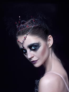 Portrait of the ballerina in the role of a black swan on black studio background. The face close up