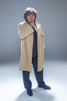 The senior man in cloak as detective or mafia boss. Studio shot on gray in retro stile