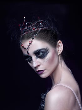 Portrait of the ballerina in the role of a black swan on black studio background. The face close up