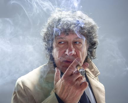 The senior man in cloak with cigar as detective or mafia boss. Studio shot on gray in retro stile