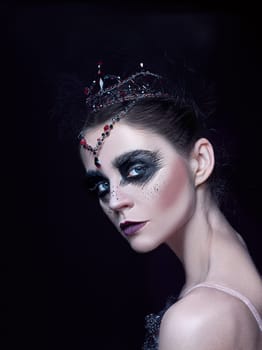 Portrait of the ballerina in the role of a black swan on black studio background. The face close up