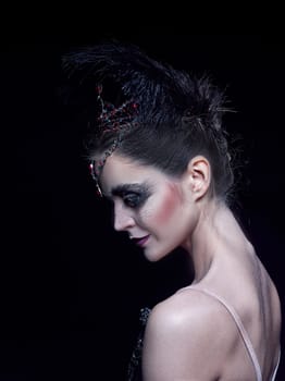 Portrait of the ballerina in the role of a black swan on black studio background. The face close up