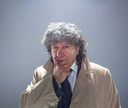 The senior man in cloak as detective or mafia boss. Studio shot on gray in retro stile