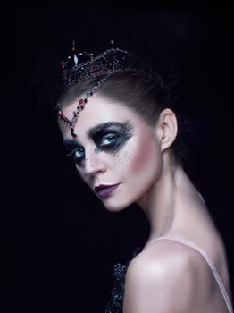 Portrait of the ballerina in the role of a black swan on black studio background. The face close up
