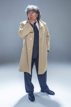 The senior man in cloak as detective or mafia boss. Studio shot on gray in retro stile