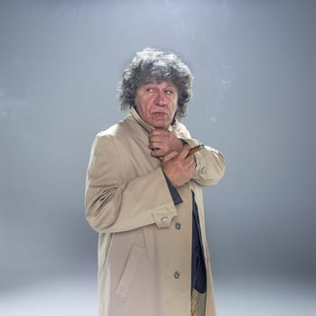 The senior man in cloak with cigar as detective or mafia boss. Studio shot on gray in retro stile