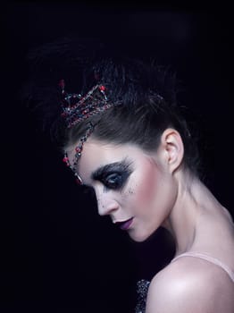 Portrait of the ballerina in the role of a black swan on black studio background. The face close up