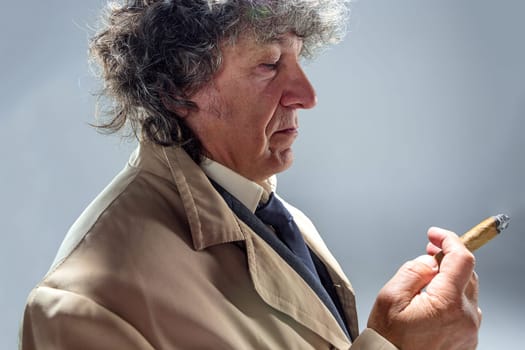 The senior man in cloak with cigar as detective or mafia boss. Studio shot on gray in retro stile