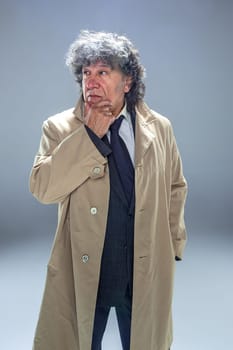 The senior man in cloak as detective or mafia boss. Studio shot on gray in retro stile