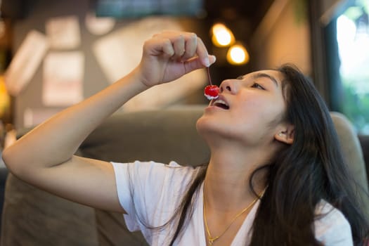 Beautiful Asian girl is eating cherry in cafe.