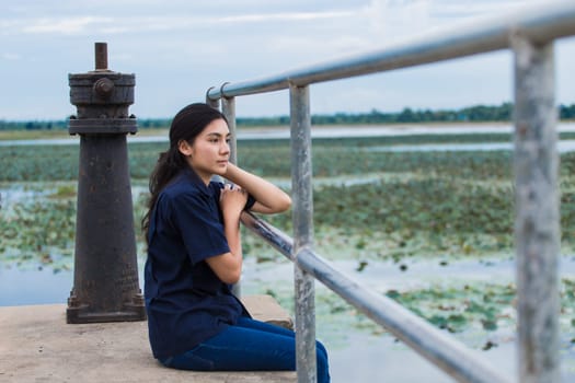 Young beautiful Asian girl sitting on jetty forest and river on background