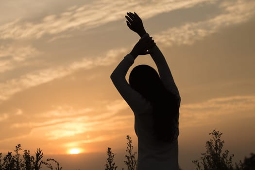 Silhouette of a young asian woman enjoying flowers and nature sunset