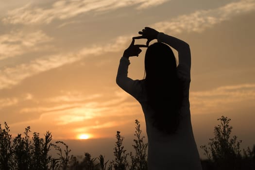 Silhouette of a young asian woman enjoying flowers and nature sunset